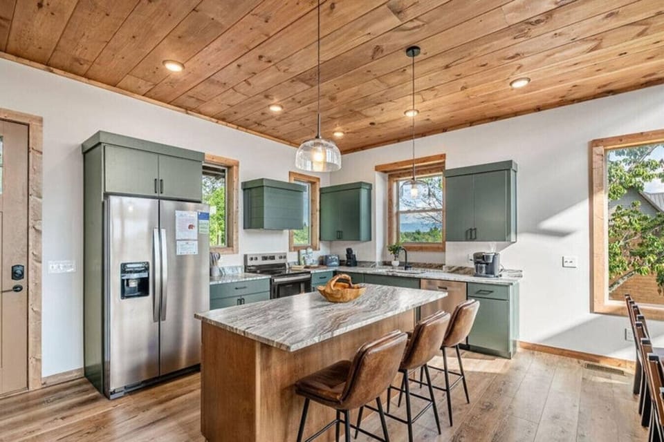 Sage green cabinetry, warm wood ceilings, and a spacious island create a kitchen that’s both stylish and functional. Cook, prep, and snack while sunlight pours in from every angle.