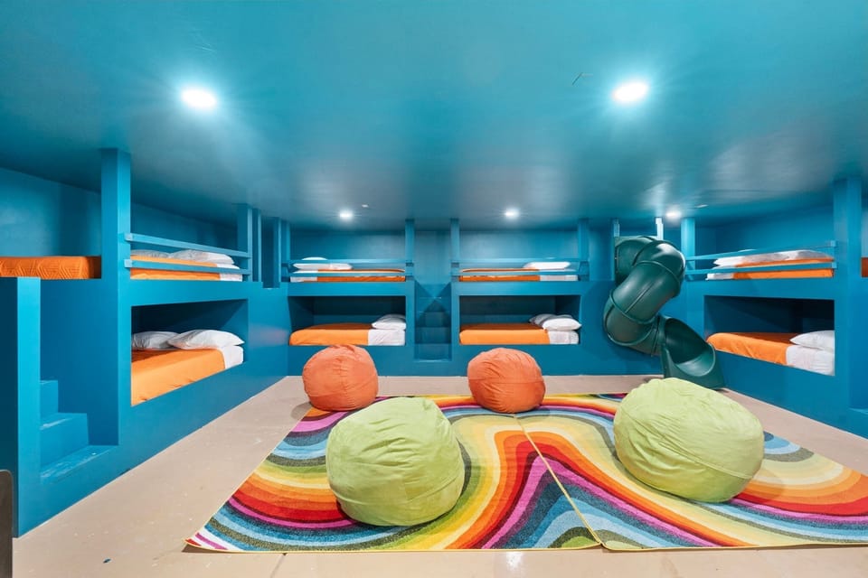 Playful bunk/game room with beanbags, arcade machines, slide, and bright colors.
