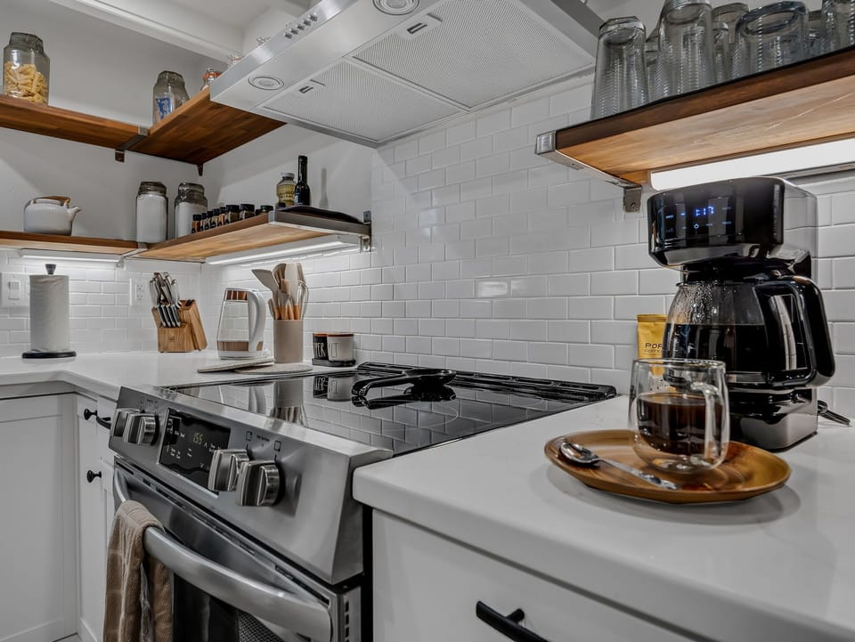 Enjoy a morning coffee station setup right on sleek white countertops next to a modern gas range and oven.
