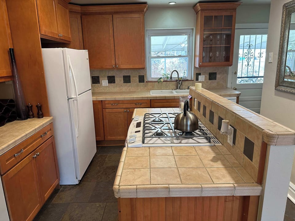 Traditional kitchen with oak cabinetry, tiled countertops, and a central island featuring a gas range. Includes a white refrigerator and slate-colored tile flooring for a durable, homey feel.
