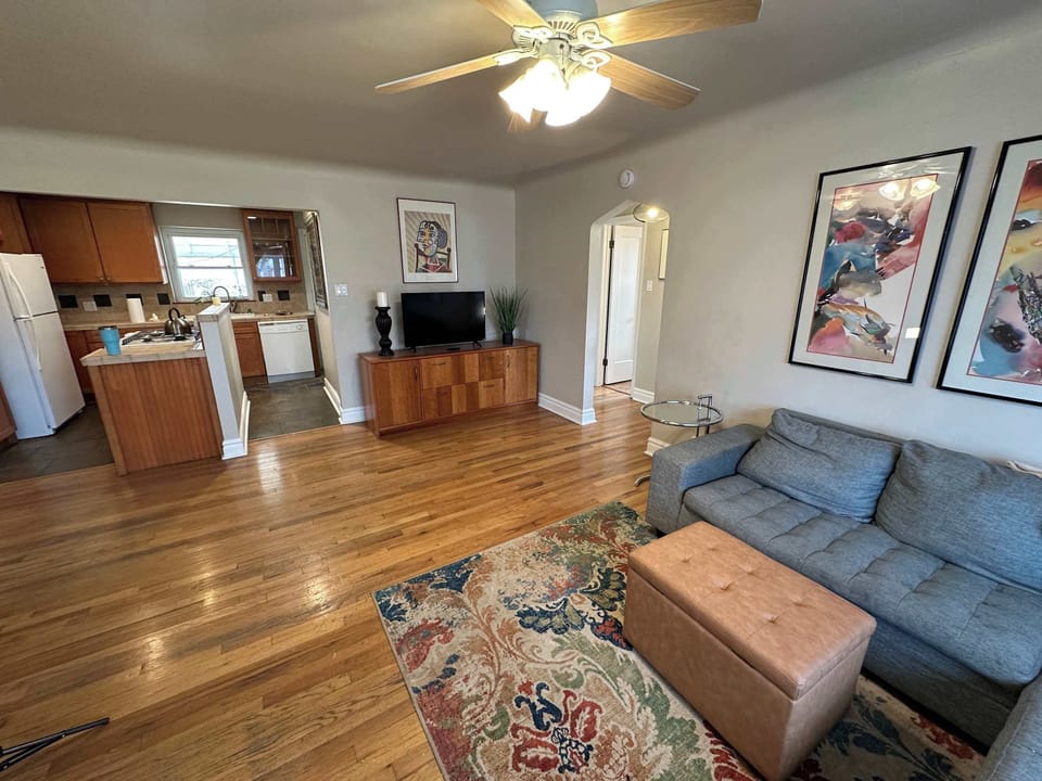 Spacious living room featuring a large sectional, vibrant area rug, and ceiling fan. The open-plan layout connects the lounge area to the kitchen and hallway, perfect for modern family living.