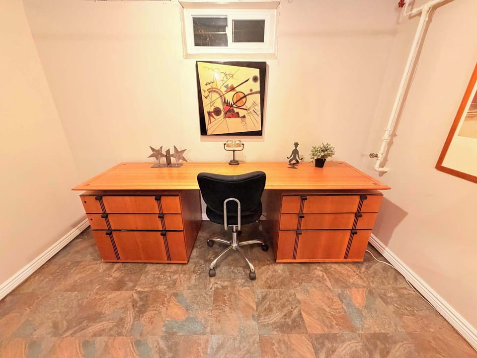 Spacious home office setup featuring a large wood desk with ample drawer storage. Abstract wall art and a professional swivel chair make this an ideal, quiet workspace for remote professionals.