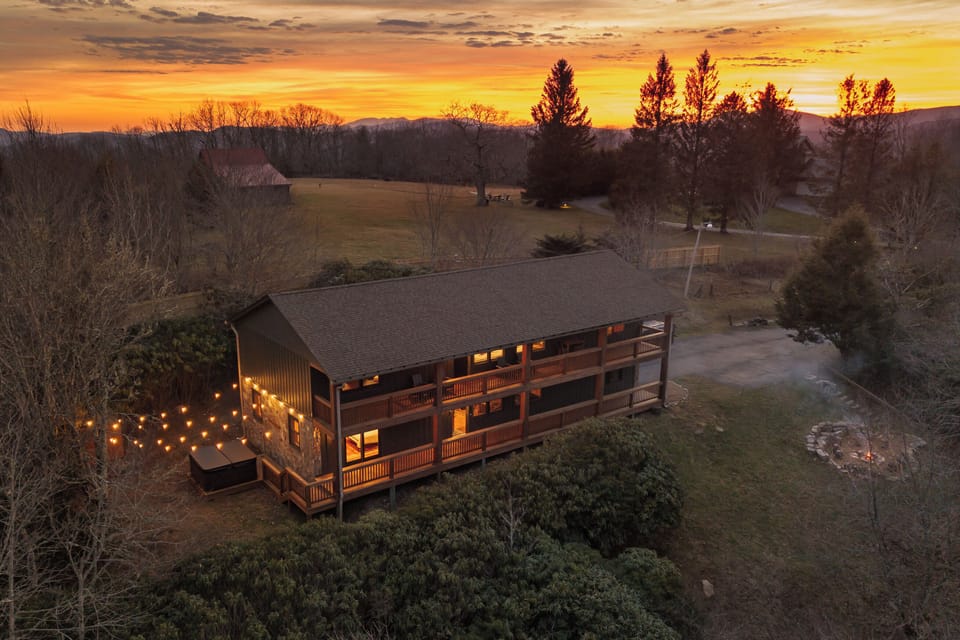 A peaceful view of the home glowing at sunset, surrounded by open meadow and evergreens. A great first impression showing the privacy, charm, and calm setting guests can expect during their stay.