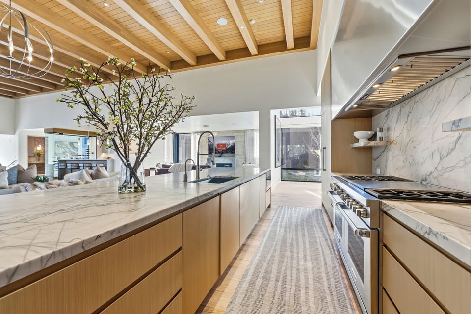 Bright modern kitchen with minimalist cabinetry, large island, and full views into the dining and outdoor living areas.