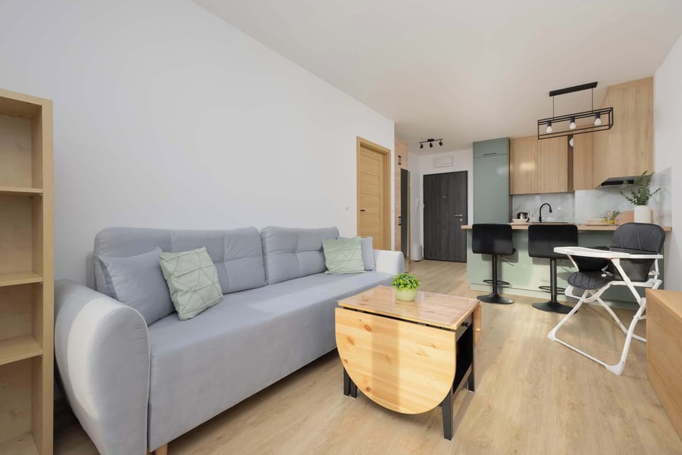 Cozy living area with a grey sofa, wooden accents, and soft natural light from the window.