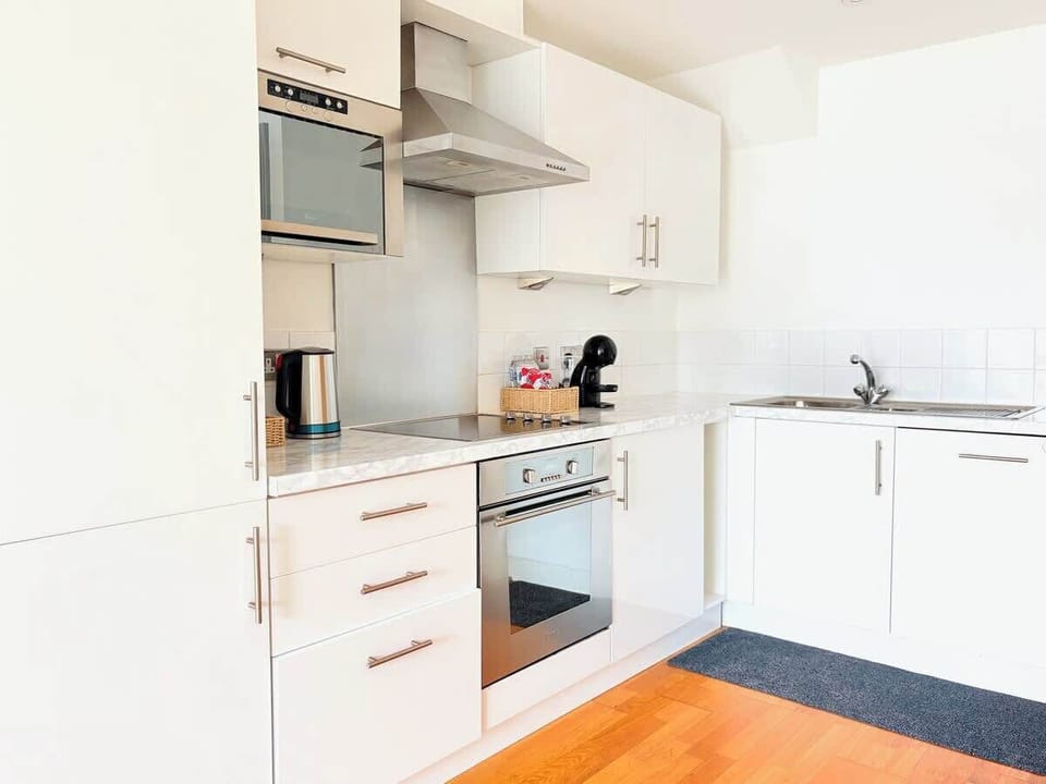Open, light-filled layout connecting kitchen and hallway with warm wooden flooring, modern white units, and open sight-lines to living areas. Functional and welcoming design perfect for guests seeking space and style in York.