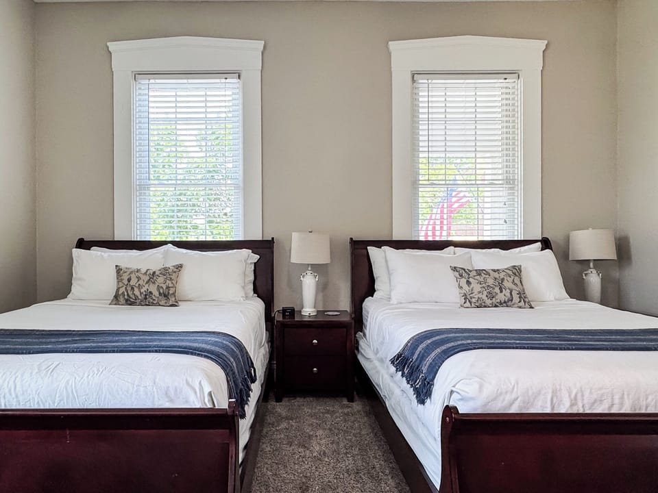 Spacious main level bedroom includes two plush queen size beds with crisp white linens and a full bathroom with combo tub and shower off the hallway at Aussie Cottage.
