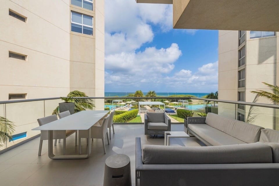 Modern beachfront balcony with sweeping ocean views, lush gardens, and sparkling pools. Unwind in sleek seating and dine al fresco as tropical breezes surround you.