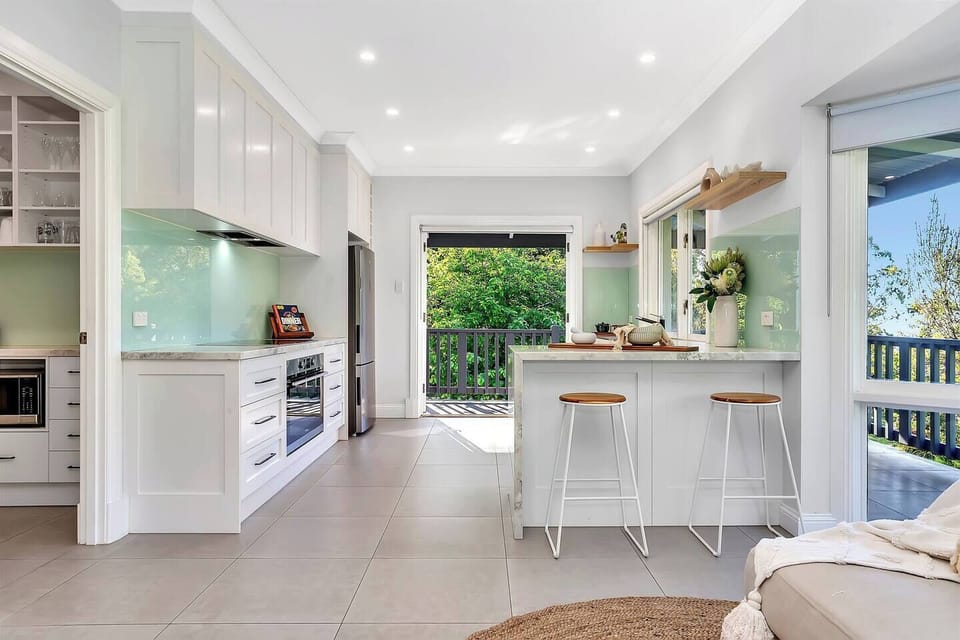 This gourmet kitchen pairs modern appliances with a breakfast bar and stools, opening seamlessly to treetop views.