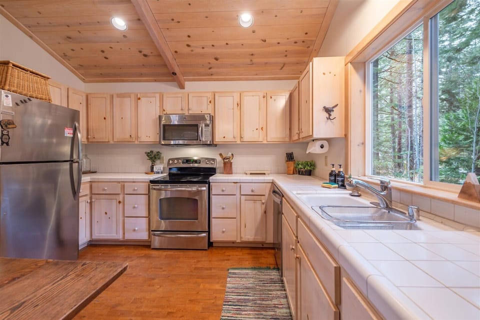 Your fully equipped kitchen welcomes you with warm wood cabinetry and modern appliances, perfect for preparing meals while enjoying views of the surrounding forest through large windows.