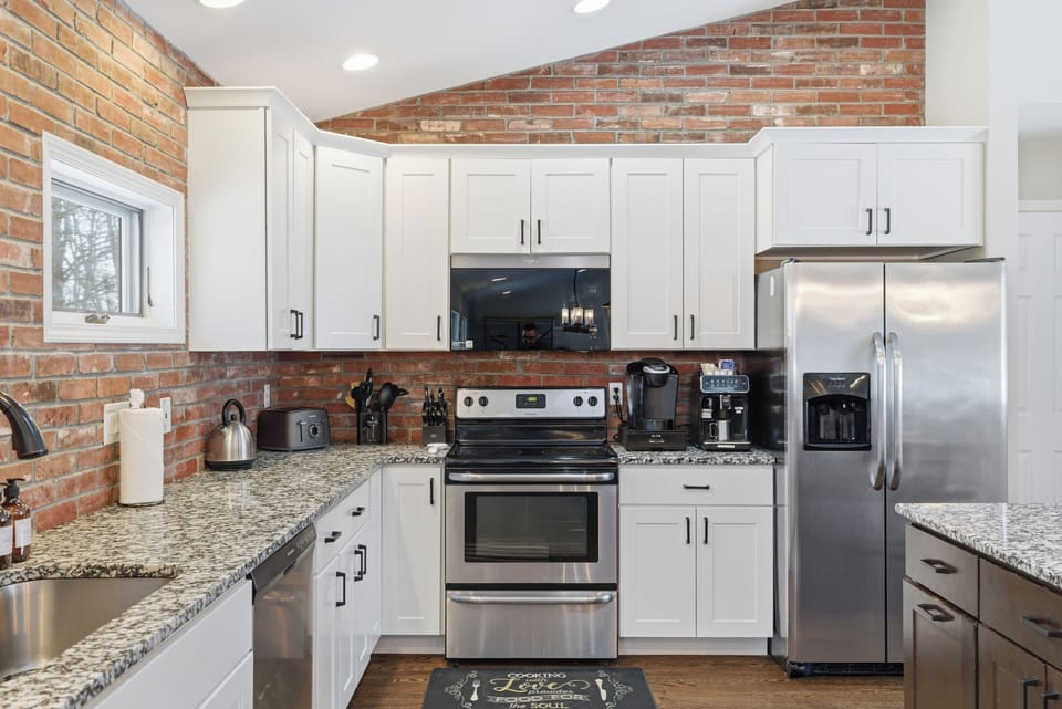 Fully stocked kitchen with stainless appliances and warm brick accents.