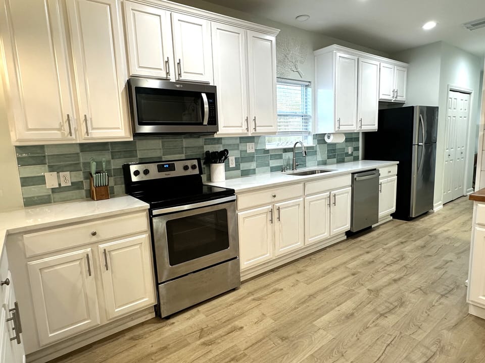 White cabinets, blue-green backsplash, stainless steel appliances, bright light.