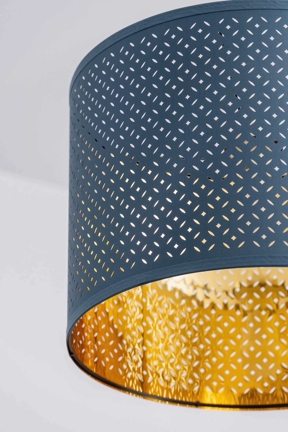 Modern perforated lampshade in deep blue with a golden interior, casting warm and decorative light patterns around the room.