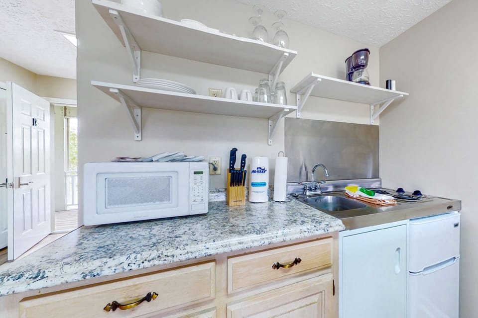 Kitchenette with microwave, sink, cooktop, mini fridge, coffee station, and essentials. Great for extended stays and quick meals. Practical studio amenities for easy, comfortable travel.