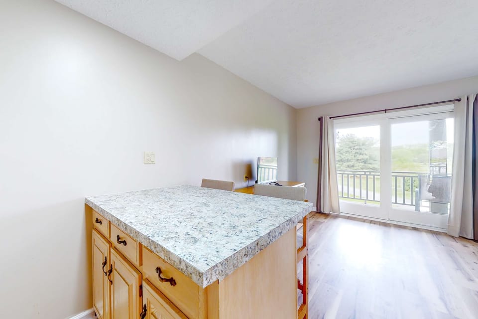 Kitchen island with open living space and sliding door to balcony. Bright, airy studio setup for couples, remote work, and extended stays. Comfortable studio unit with outdoor access and views.