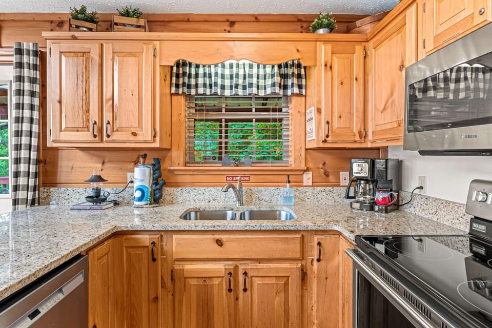 Fully equipped rustic cabin kitchen with granite countertops, stainless appliances, custom wood cabinetry, and farmhouse charm.