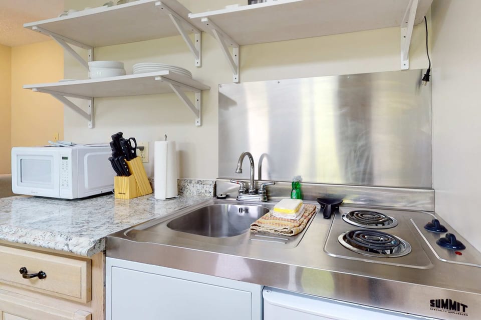 Compact cooktop kitchenette with sink, microwave, mini-fridge & essentials. Cook and save on dining out. Budget-friendly condo, self-catering, long stays, extended stay, convenient for travel & work.
