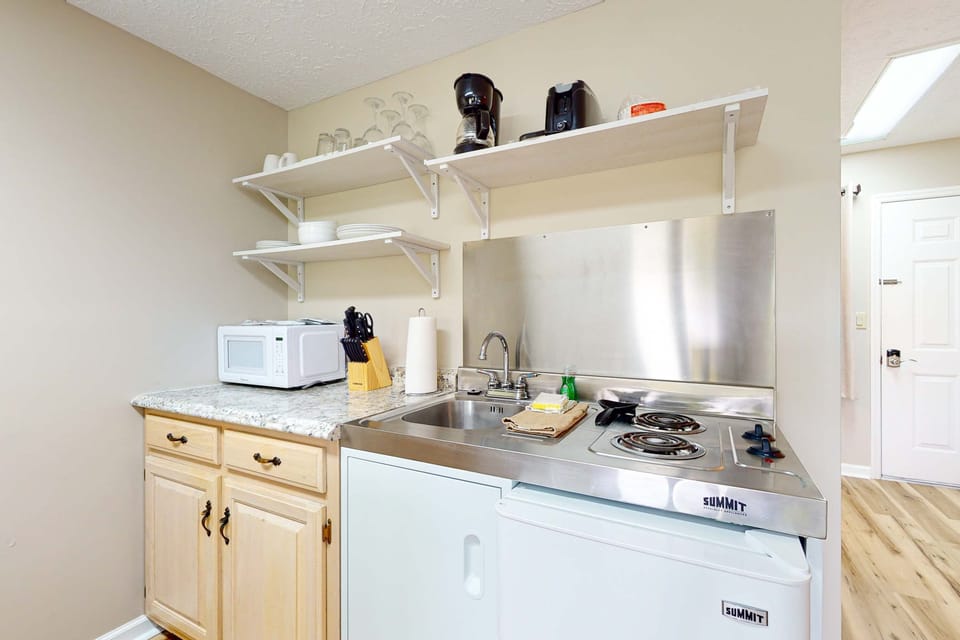 Compact kitchenette with cooktop, mini fridge, microwave, sink, coffee maker, dishes & cookware. Ideal for long stays, weekend getaways, and budget-friendly studio and travel with easy meals.