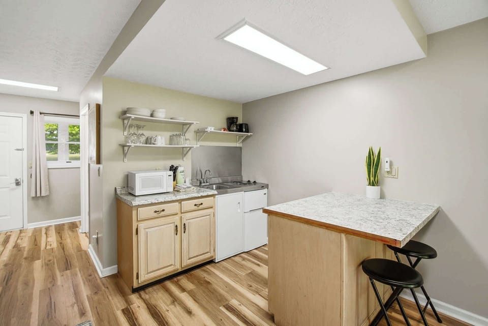 Kitchenette with breakfast bar seating, microwave, sink, cooktop, and coffee setup. Perfect for long stays and quick meals. Budget-friendly space with practical amenities and comfort.