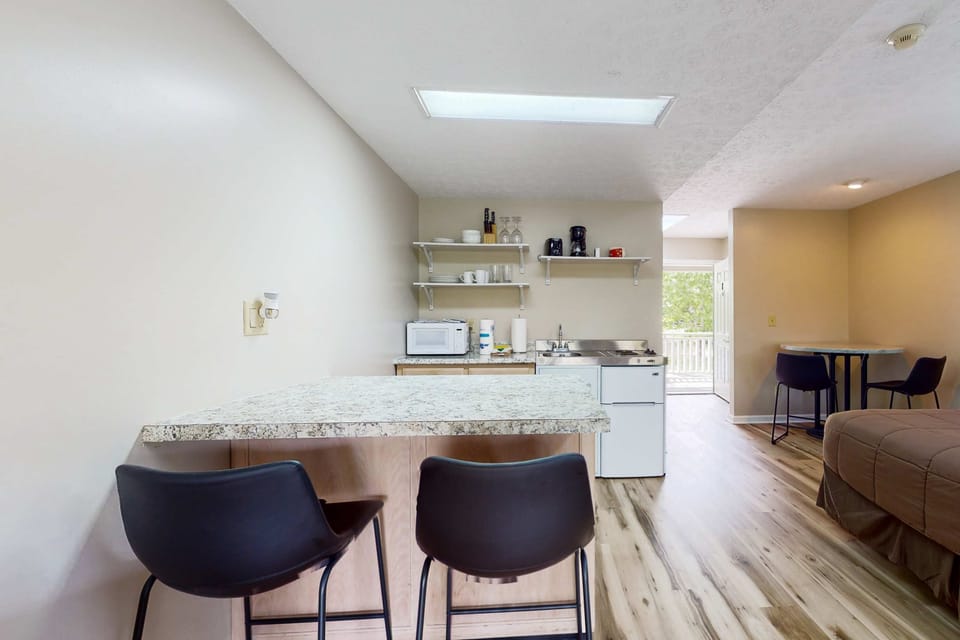 Breakfast bar seating beside kitchenette. Great for coffee, quick meals, and work travel. Studio suite with mini kitchen, microwave, sink, fridge, dishes, and convenient dining space.
