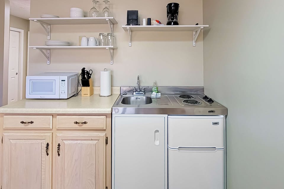 Kitchenette with cooktop, mini-fridge, microwave, coffee maker, sink, dishes & glassware. Perfect for extended stay, work travel, golf getaway, and budget-friendly lodging with easy meal prep.
