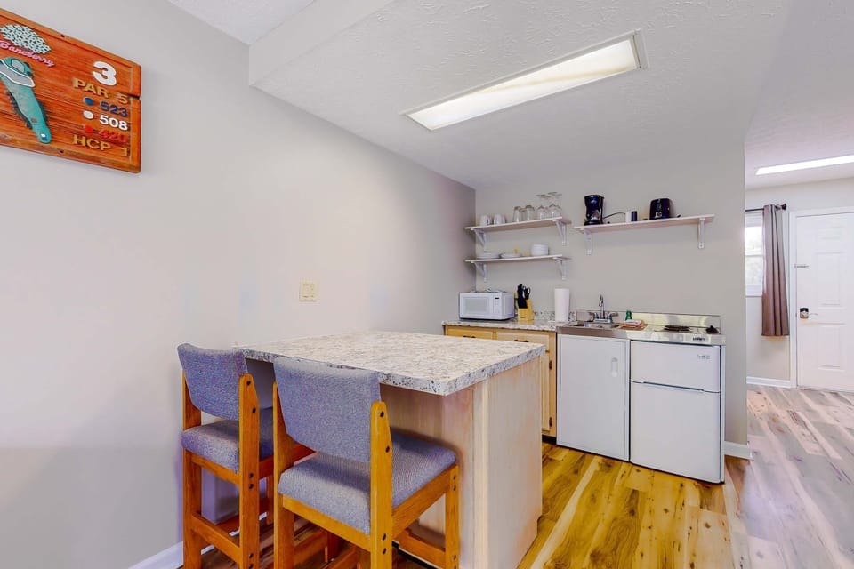 Kitchenette with breakfast bar seating, microwave, mini fridge, sink, dishes, coffee maker, easy meals for extended stays. Clean, bright studio suite ideal for short trips, weekend getaways, and families.