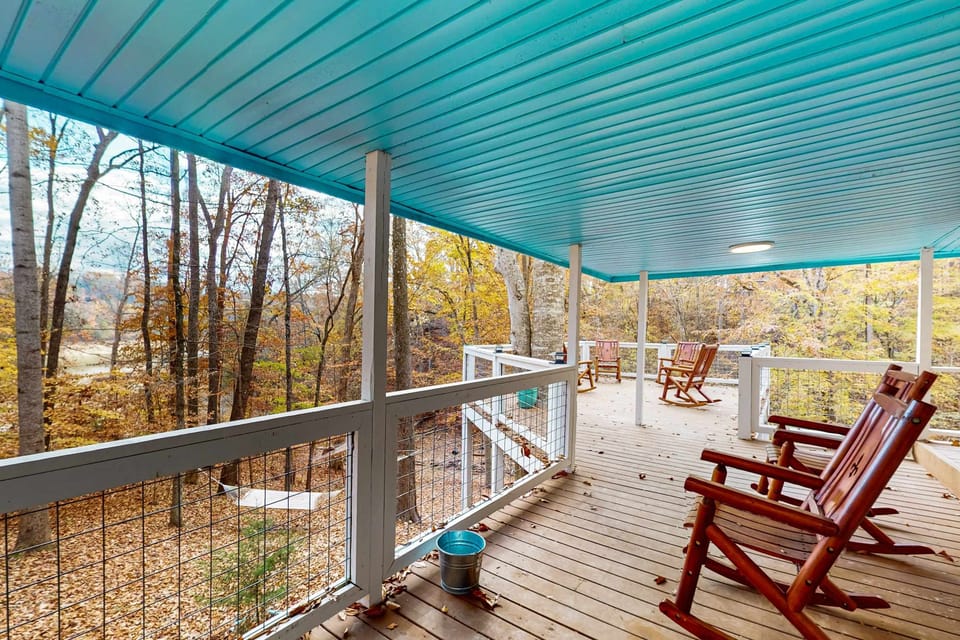Large covered wraparound deck with rocking chairs and peaceful wooded views, perfect for relaxing outdoors.