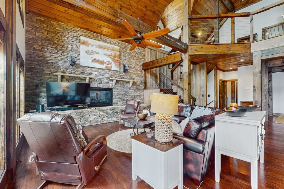 Gather in this grand living room featuring a stunning stone fireplace, vaulted ceilings, and cozy seating. Ideal for luxury cabin stays and group getaways.