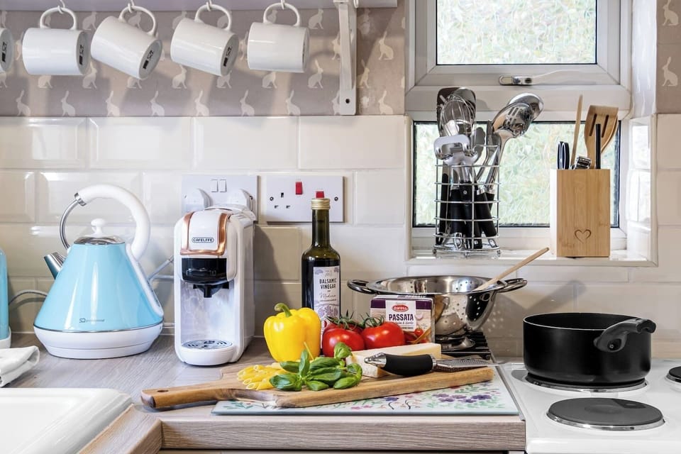 A styled kitchen counter with kettle, coffee machine, cookware, and ingredients.