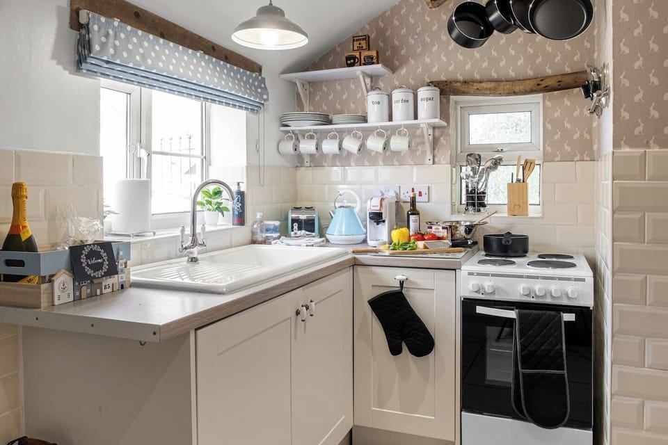 A kitchen corner showing the sink, worktops, shelving, and cooker.
