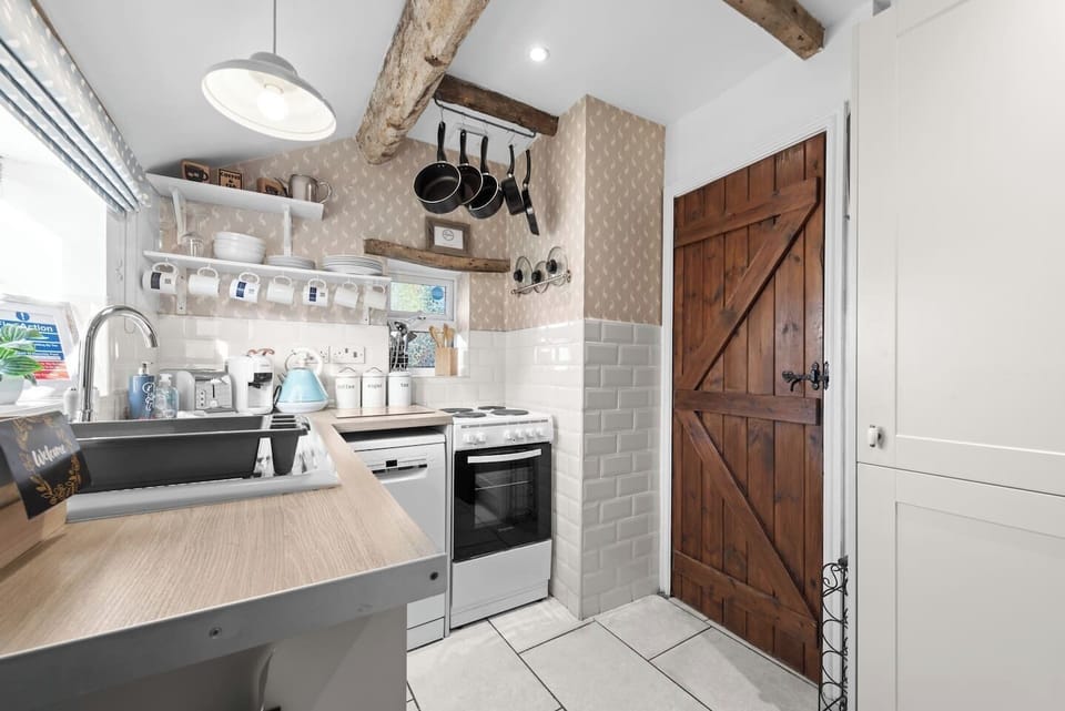 A bright kitchen view with wood beams, open shelving, and a wooden door.