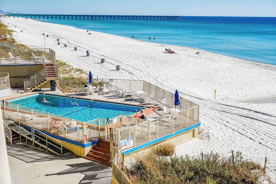 The beachfront studio offers a stunning view of the white sand beach and the sparkling turquoise waters of Panama City Beach, complete with a refreshing swimming pool surrounded by loungers for relaxation.