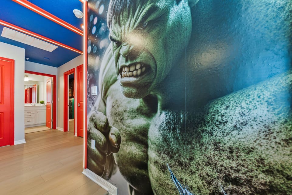Superhero hallway with a bold Hulk mural, red doors, and LED accents-follow the glow to more themed fun throughout the home!