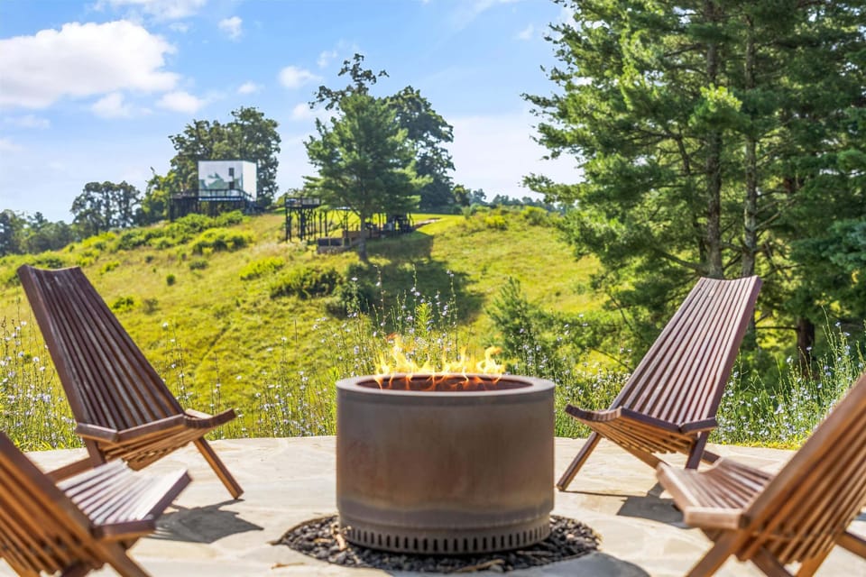 Inviting fire pit setup with wooden chairs overlooking peaceful rolling hills and open nature views.