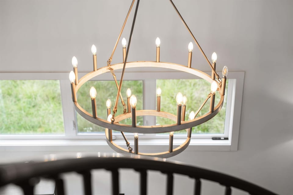Modern circular chandelier lighting fixture above staircase with large windows in background.
