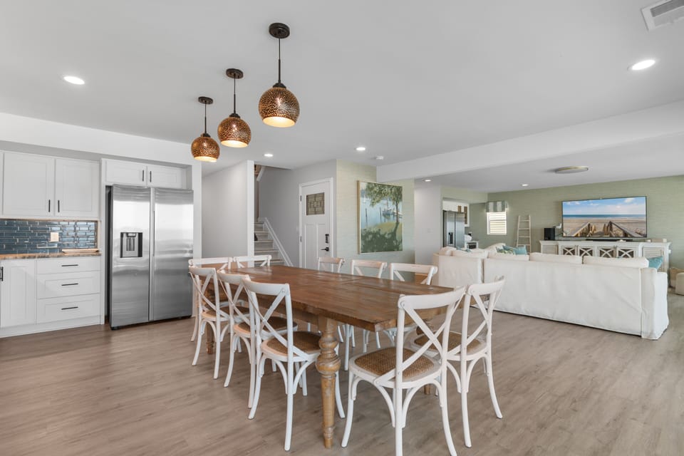 Gather around this spacious farmhouse table beneath charming pendant lights. The open layout connects your kitchen and living area, making it easy to cook, dine, and relax together in coastal style.