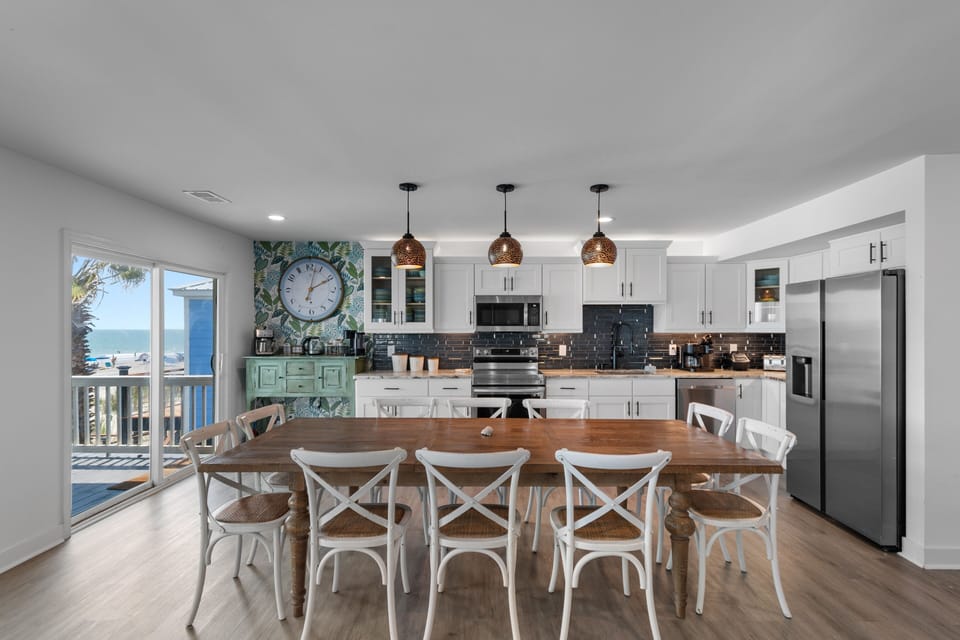 Gather around the spacious dining table in your bright, fully-equipped kitchen. Through the open doors, glimpse the beachfront awaiting you—perfect for morning coffee or planning your next coastal adventure.