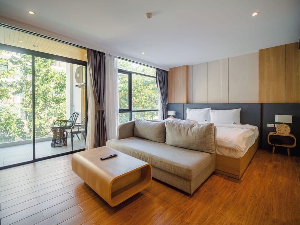 Open living space with a sofa bed and direct access to a balcony, offering views of lush green surroundings.