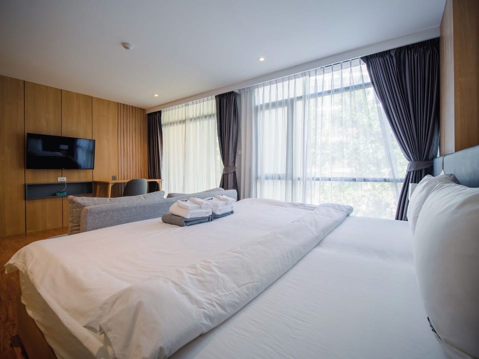 Spacious bedroom featuring a large bed, wall-mounted TV, desk area, and floor-to-ceiling windows.