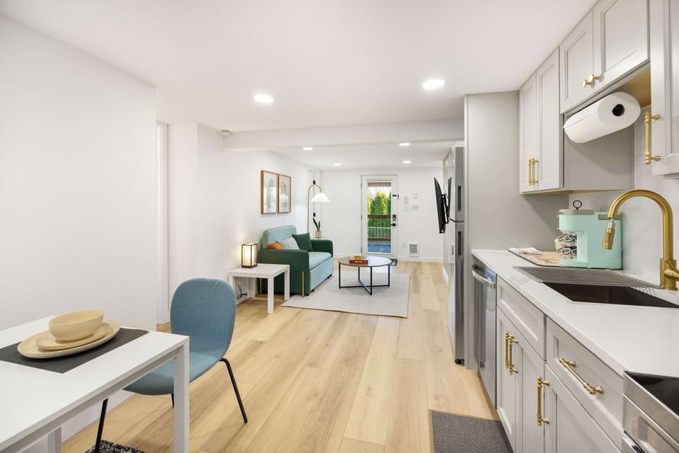 The bright and spacious living area connects seamlessly with the kitchen, featuring a comfortable sofa, warm lighting, and a TV for entertainment.