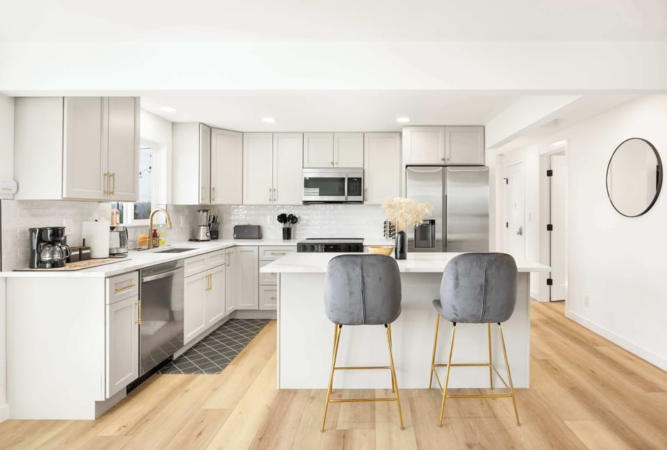 A chef’s dream! This fully equipped kitchen features sleek white cabinetry, stainless steel appliances, and elegant gold accents. The island with plush barstools is great for casual meals or morning coffee.