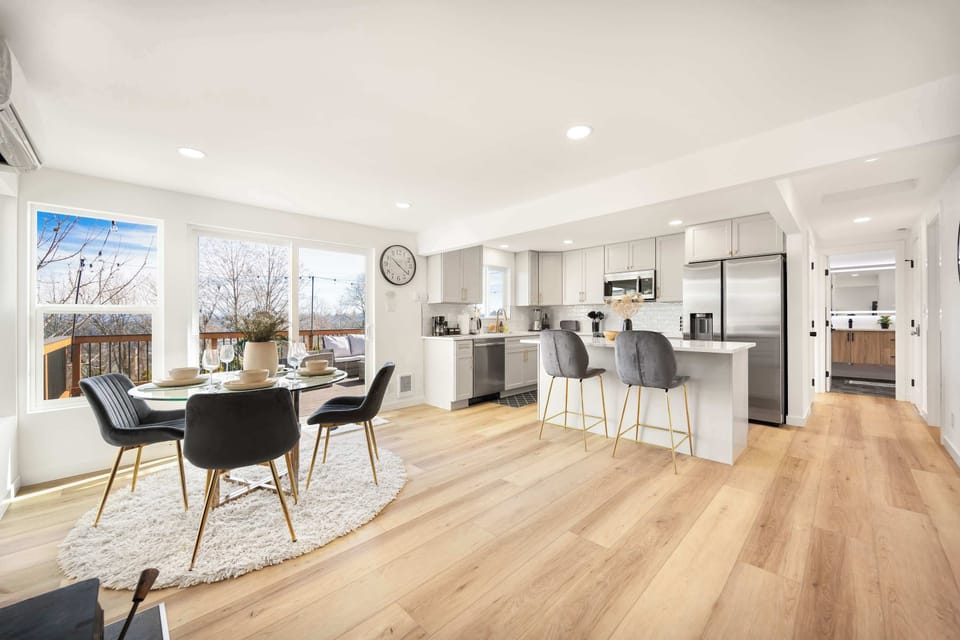 A bright and airy living space featuring a cozy dining area, a sleek kitchen with gold accents, and bar seating—perfect for enjoying meals with a view. Large windows bring in plenty of natural light!