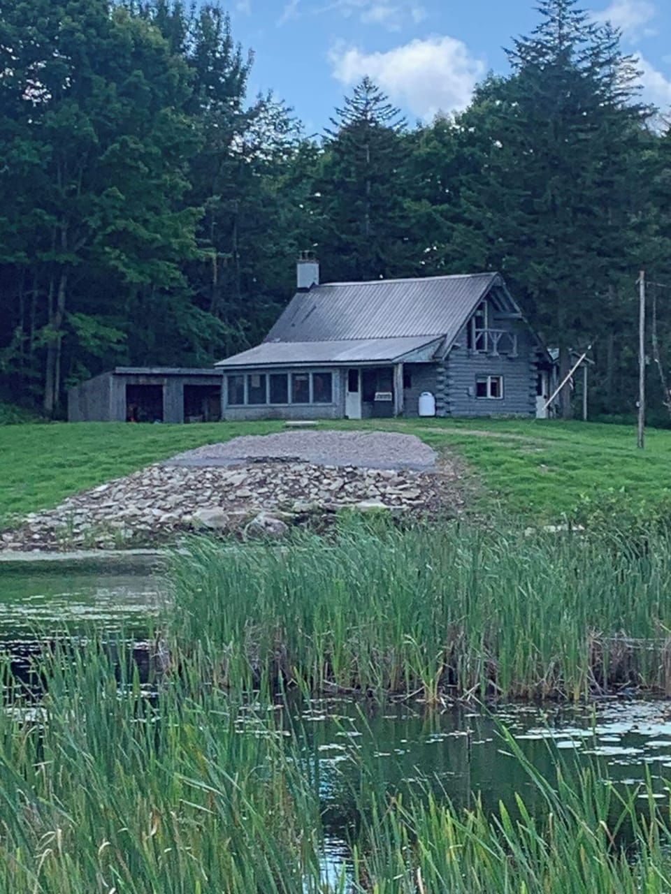 View of the cabin with the firepit & cascading stones down to the pond.