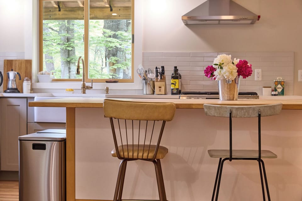 Bright kitchen with a butcher block island, bar seating, and lush forest views.