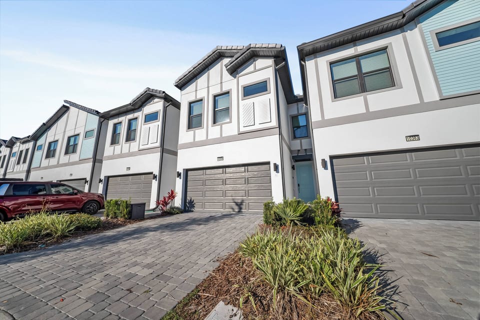 Step into this charming vacation home with its clean lines and modern façade, featuring large windows that invite natural light. The stylish brick driveway leads you to a warm and welcoming entry, surrounded by lush landscaping.