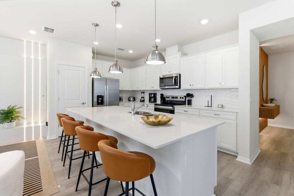 Discover this chic kitchen with sleek white cabinetry and a spacious island ideal for casual dining. The warm-hued bar stools enhance the modern appliances, crafting a perfect blend of style, function, and inviting ambiance.