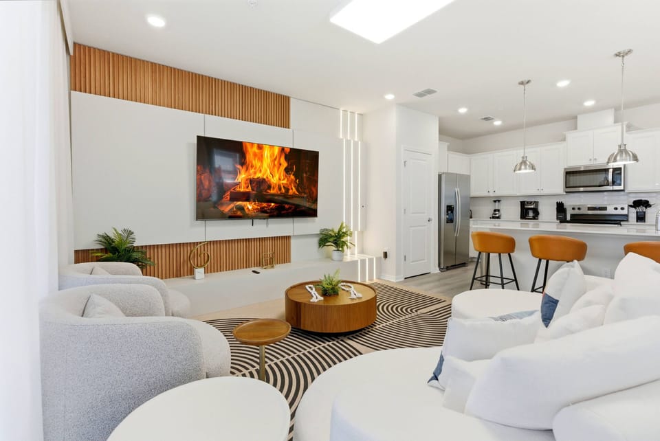 This bright and airy living space, with its soft neutral palette and warm wood accents, invites you to relax on plush white sofas by the modern fireplace or enjoy time together around the stylish round coffee table.