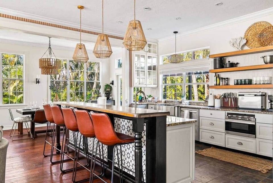 Showstopping kitchen island with butcher block top, Moroccan tile panels, leather barstools, and rattan pendants above lush garden views.