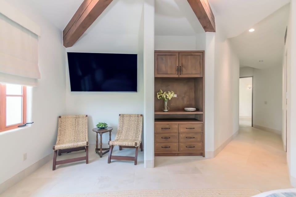 Spacious bedroom featuring vaulted wood beam ceilings, wicker chairs in a luxury Cabo vacation villa.