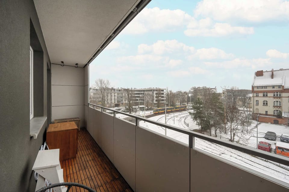 A balcony with a small outdoor seating area, offering a comfortable place to relax. The view spans residential rooftops. The space feels bright and open.